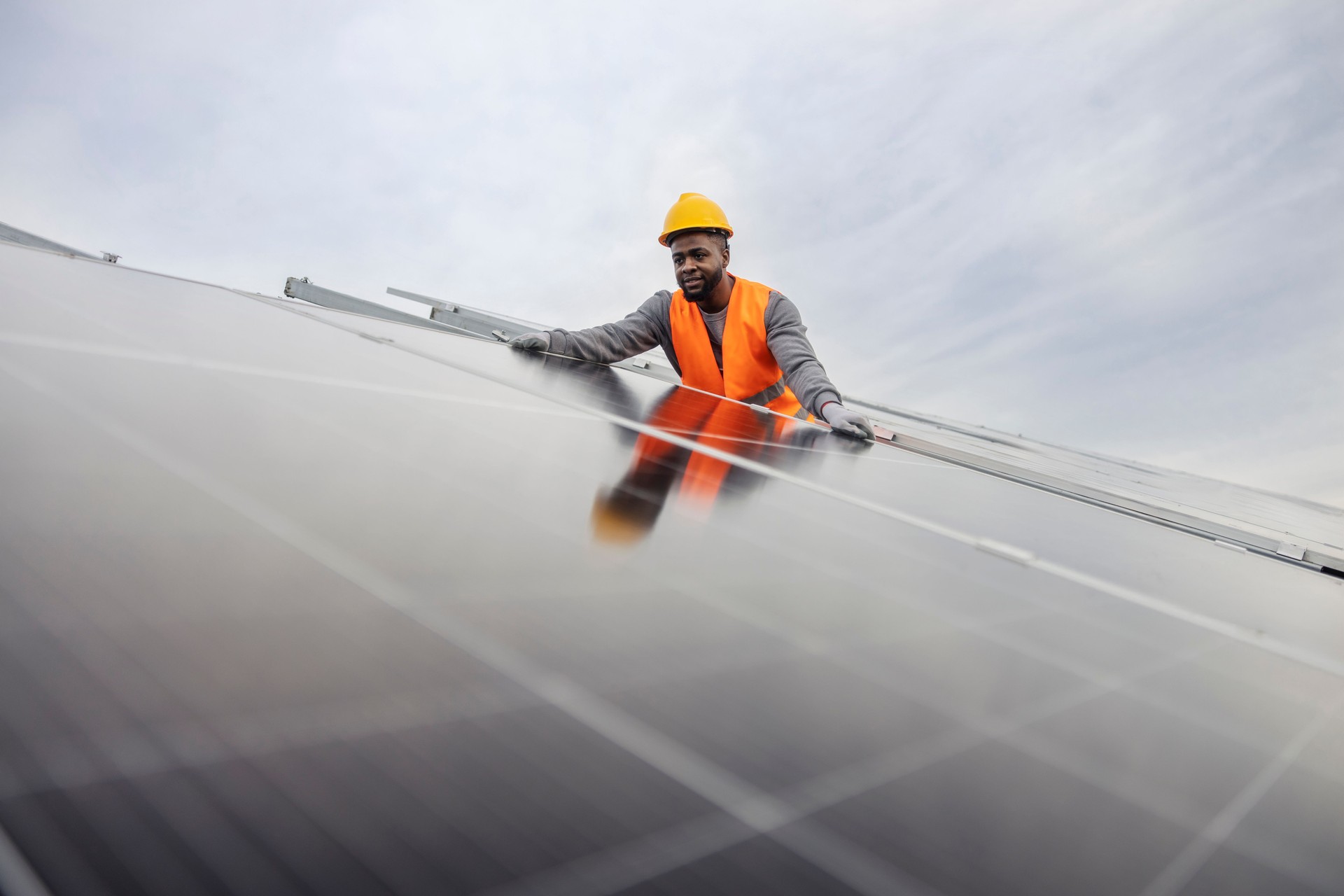Interracial hardworking black migrant worker installing solar panels at solar farm.